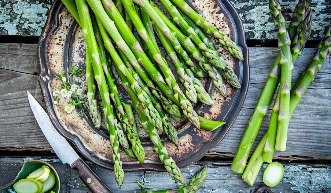 Overhead of high-fiber asparagus spears on a vintage plate against a rustic wooden board. 