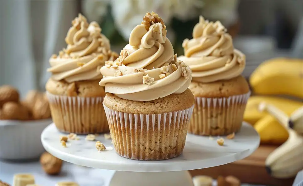 A trio of succulent vegan banana muffins topped with swirls of peanut butter cream frosting and nuts. 