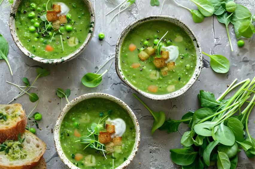 Top view of three creamy bowls of vegan split pea soup topped with croutons, sprouts, and organic sour cream.   