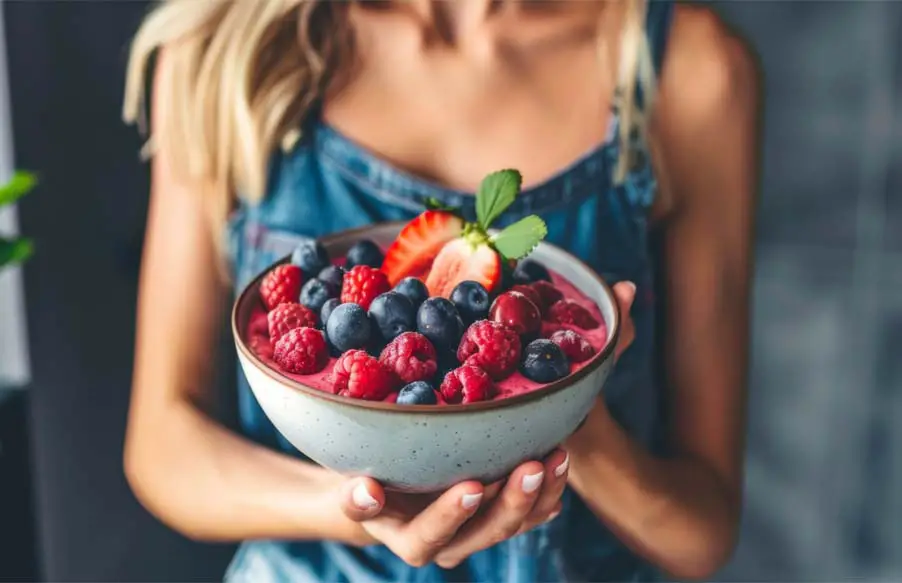 A young woman holding a colorful bowl of assorted berries.