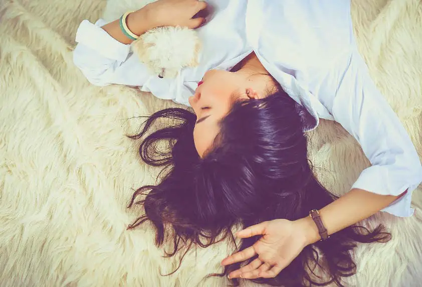 Top view of a woman sleeping with her dog on a fluffy rug.