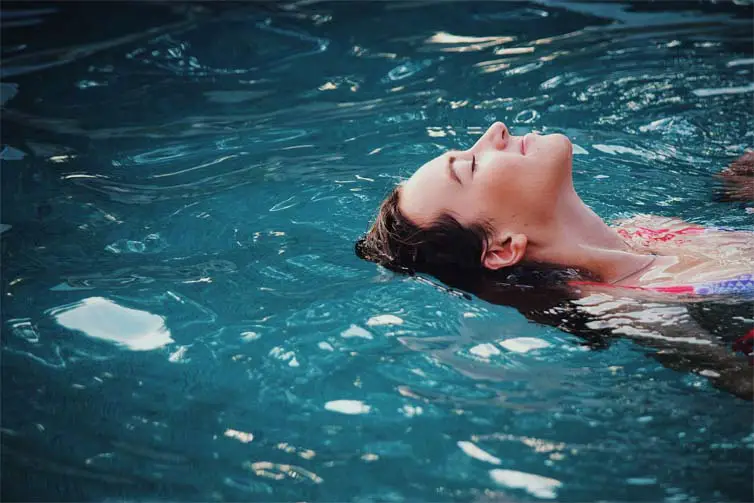 A woman in a pool peacefully  floating on her back.  