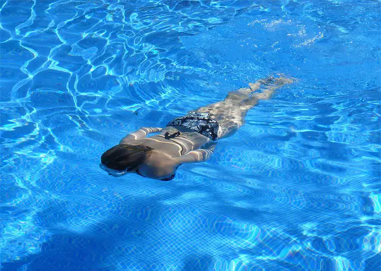 A woman gliding underwater in a deep blue swimming pool. 