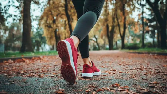 A woman running on a path with autumn leaves on the ground. 